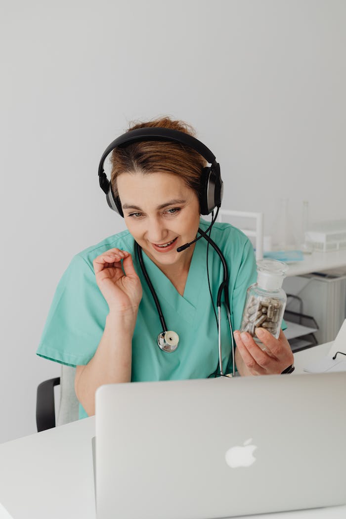 Female doctor in scrubs providing a telemedicine consult with a laptop and headset.